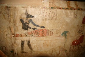 Le dieu Anubis, à tête de chacal, se tient près d’une momie. Il est le dieu de l’embaumement et le protecteur des nécropoles. Tombe de la XXVIe dynastie.