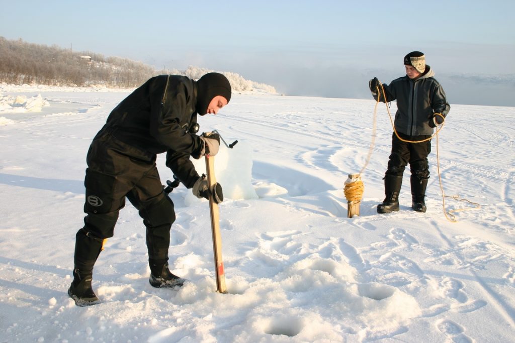 Norway. King crab fishing. Sawing ice to make a diving hole. 