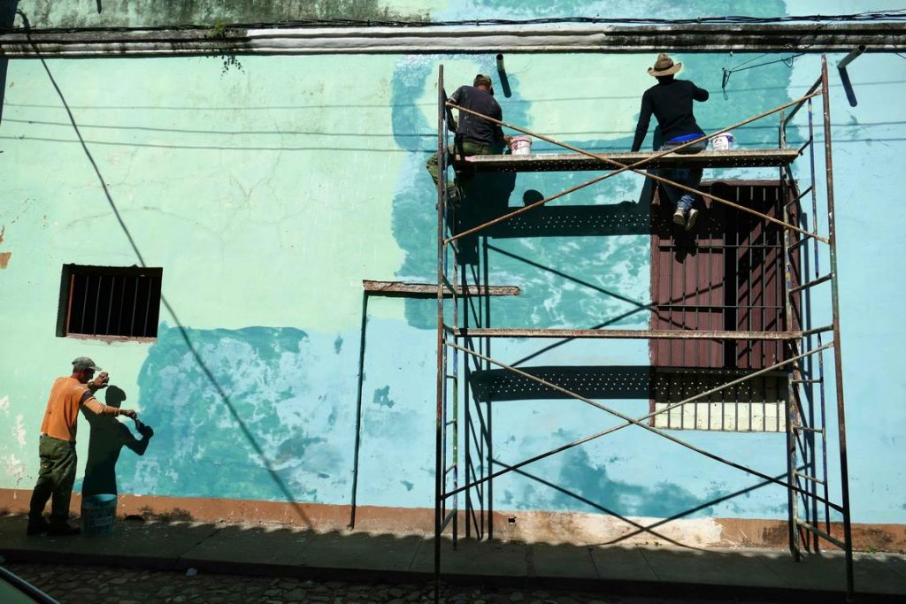 Trinidad. Perched on makeshift scaffolding, these painters were able to recover paint to partially renovate the façade.