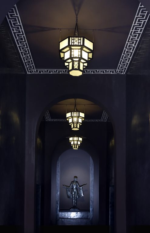 Marrakech. Villa Makassar. La porte sur rue, sculptée dans le cèdre et l’acajou, ouvre sur un long couloir de mystérieuse pénombre au bout duquel veille une statue de bronze.