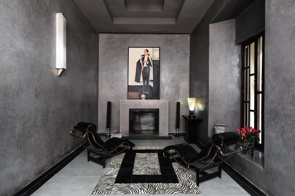 Marrakech. Villa Makassar. De part et d’autre de la cheminée, des fauteuils de Le Corbusier, éclairés d’appliques Jean Perzel regardent le personnage emblématique du salon : le Maharadja d’Indore, ici reproduit d’après un tableau de Bernard Boutet de Monvel.