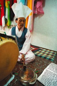 Corée du Sud. Rituel chamanique ou kut. Alors que les assistants se frottent la paume des mains en signe de recueillement, les musiciens commencent à frapper tambours et cymbales sur un rythme vif et insistant.