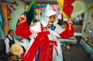 Corée du Sud. Rituel chamanique ou kut. Tour à tour, la chamane brandit des sabres ou des drapeaux, agite un bouquet de tiges de riz, sert de l’alcool, lance du riz pour apporter le bonheur.