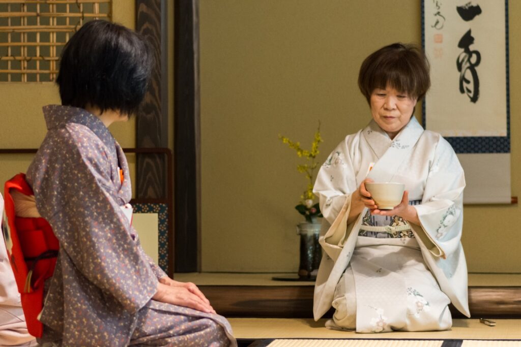 Japan. Tea ceremony. The tea mistress presents the bowl of matcha and offers it to her guest, holding it in both hands.