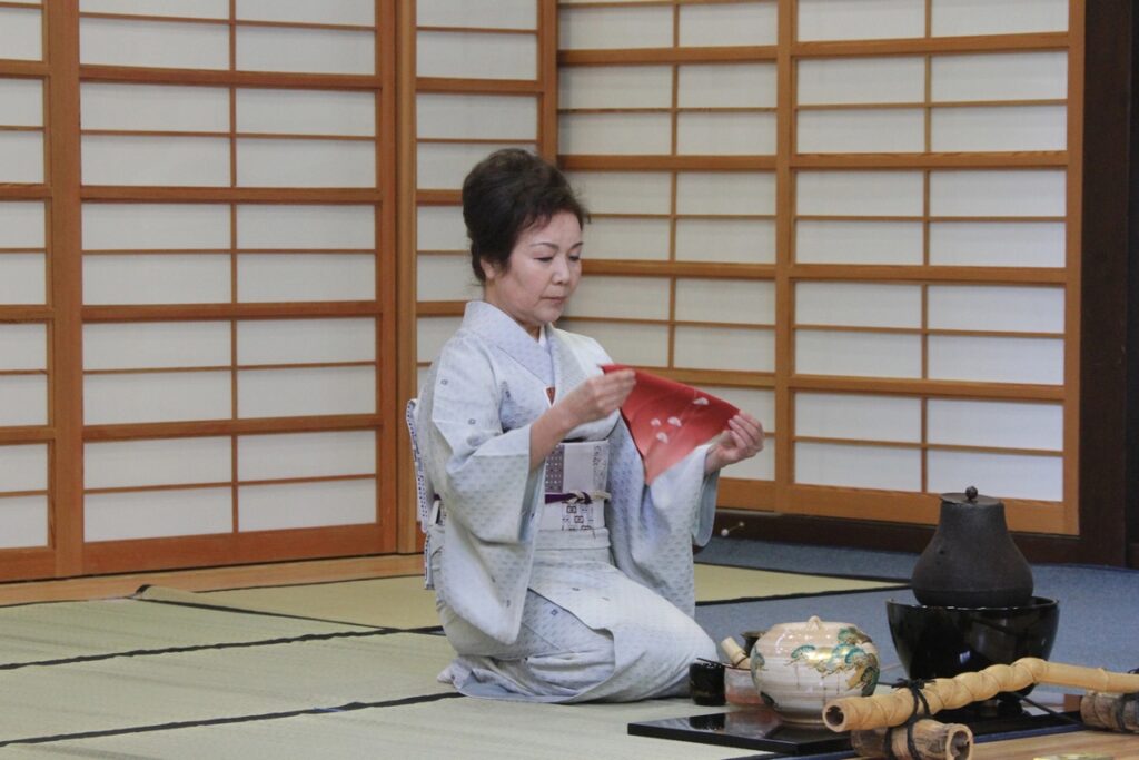 Japan. The tea master takes a red linen cloth (fukusa) from her obi (the wide belt of the kimono), folds it into a triangle and folds it over herself in a highly codified gesture.