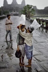 Cambodia. Angkor Wat. Children using plastic bags to protect themselves from the rain. Steve McCurry.